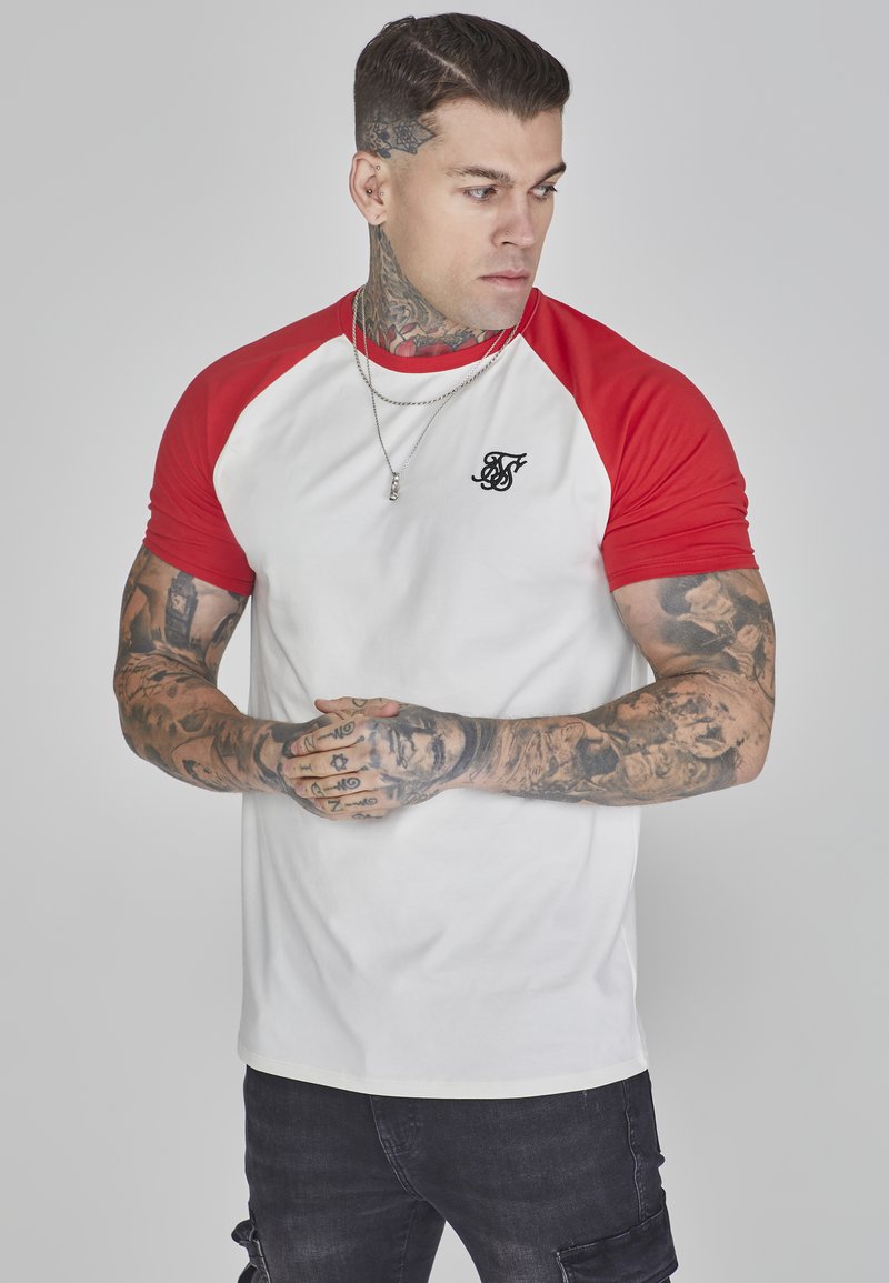 Tricou raglan roșu și alb cu mâneci scurte, guler rotund, având un logo mic negru pe piept; țesătură din bumbac neted, design fitted.