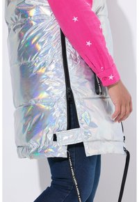 Glanzend zilveren opblaasvest met horizontale naden, zijritsen en een reflecterend oppervlak. Gecombineerd met een roze langemouwen top met witte sterren.