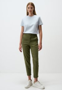 T-shirt azzurro chiaro a maniche corte abbinato a pantaloni olive verdi a sigaretta, con chiusura frontale a bottoni e sneakers bianche. Design semplice, texture liscia.