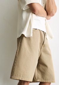 Beige bomulds shorts med en afslappet pasform, der har synlige syninger og sidelommer, parret med en lysfarvet struktureret over skjorte.