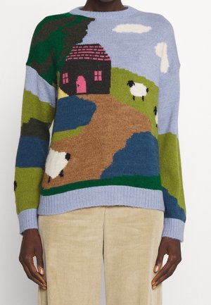 Svetr s krajinným vzorem pletení znázorňujícím hnědou cestu vedoucí k černému domu s růžovými dveřmi, zelené kopce, modrou oblohu, bílé mraky a ovce.