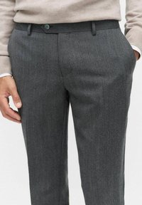 Grå dressbyxor i texturerat tyg. Har en slät framsida, sidfickor och knappstängning. Bärs med en beige tröja.