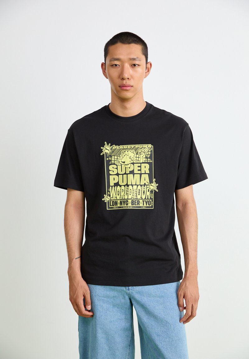 Black cotton t-shirt featuring a large yellow graphic print with "SUPER PUMA WORLD TOUR" and plant motifs, paired with light blue jeans.