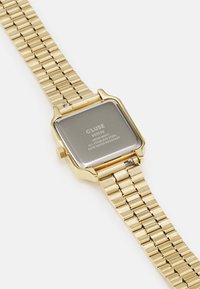 Montre en acier inoxydable doré avec un boîtier carré, un bracelet en maille métallique et un dos gravé, dotée d'une résistance à l'eau et d'un mouvement japonais.