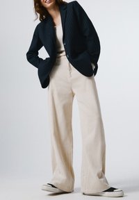 Blazer a rayas marinas, top de punto color crema, pantalones de pana anchos en color marfil y zapatillas con detalles en negro. Texturas suaves y ajuste estructurado.