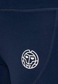 Leggings blu navy realizzati in tessuto elastico presentano un logo circolare bianco con un design facciale sulla coscia, in contrasto con il materiale.