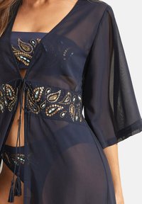 Veste légère marine avec des manches courtes évasées, ornée d'ornements dorés et turquoise complexes au niveau de la taille et dotée d'une fermeture à cordon.