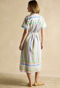 Gestreiftes Baumwollkleid mit kurzen Ärmeln, tailliert mit einem Gürtel, in Pastellfarben wie Rosa, Grün und Blau. Sandalen mit gelben Riemen.