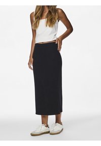 Svart ribbad midikjol med en åtsittande midja. Kombinerad med en vit tajt topp och vita sneakers med grå detaljer. Slät textur.