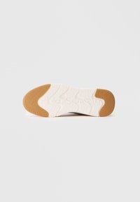 Podeszwa buta z białej gumy, wyposażona w wzór bieżnika oraz tanową gumową wstawką na pięcie i palcach dla lepszej przyczepności.