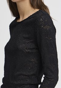 Top nero a maniche lunghe con motivi floreali testurizzati, scollatura rotonda e tessuto leggermente trasparente con una silhouette aderente.