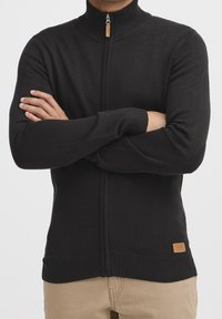 Svart zip-up tröja med hög krage, ribbade ärmslut och nederkanter. Har ett dragkedja i trä och en liten etikett på den nedre sidan.