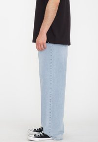 Jeans de mezclilla azul claro con corte recto, con detalles de costura, bolsillos laterales y combinados con zapatillas de lona negra.