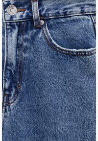 Gros plan d’un jean en denim bleu montrant la poche avant, la boucle de ceinture, le rivet en métal et les détails de couture orange.