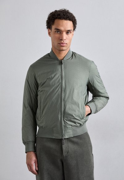Veste bomber verte en tissu texturé avec un motif subtil, dotée d'une fermeture éclair sur le devant et de poignets côtelés, associée à un pantalon vert assorti.
