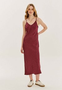 Bordová maxi šaty s výstrihom do V, tenkými ramienkami, jemným vzorom a hladkou textúrou, v kombinácii s bielymi teniskami.