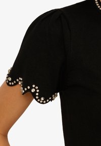 Černý pletený top s nabíranými rukávy, s vroubkovaným lemem zdobeným stříbrnými rhinestony v dekorativním vzoru.