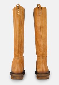 Botas altas de cuero marrón claro con una textura suave, costuras laterales y un tacón de madera apilada. Dos tiradores en la parte superior para facilitar el uso.