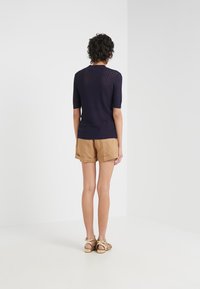 Top de punto azul marino con mangas cortas, que presenta un patrón texturizado y un diseño de espalda ligeramente abierta, combinado con shorts caqui y sandalias de tiras.