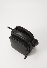 Black leather crossbody bag with two zippered compartments, rectangular shape, smooth texture, and a side fabric handle for easy carrying.