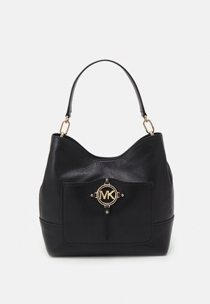 Sac à main en cuir noir avec une seule poignée supérieure, une poche avant et un emblème circulaire doré centré sur la poche.