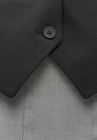 Μαύρος υφασμάτινος γιακάς με στρογγυλή μορφή και ένα μαύρο κουμπί, επικάλυψη σε έναν ανοιχτό γκρίζο υφασμάτινο ρούχο. Τα υλικά φαίνονται λεία και δομημένα.