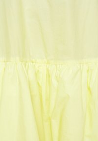 Tissu jaune clair avec une couture froncée créant une texture froncée près du bord inférieur du tissu.