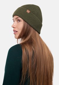 Green ribbed knit beanie with a leather patch, close-fitting design, and subtle texture, set against a plain white background.