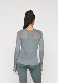 Top atlético de manga longa em tecido cinza suave. Apresenta painéis de malha nos ombros, design ajustado e buracos para os polegares nas mangas para maior conforto.