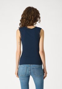 Ναυτικό μπλε αμάνικο μπλουζάκι με κομψές λευκές λεπτομέρειες στους ώμους, διαθέτει ριγέ υφή και εφαρμοστή σχεδίαση. Φοριέται με ανοιχτό μπλε τζιν.