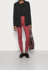 Zwarte blazer, aansluitend zwart topje, burgundy suede broek, zwarte loafers, met een burgundy handtas. Minimalistisch design met een op maat gemaakte pasvorm.