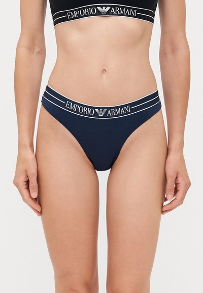Marineblauwe bikini-broekjes met een zachte elastische tailleband waarop het "Emporio Armani" logo in het wit is gedrukt. Glad stof, ontwerp met minimale bedekking.