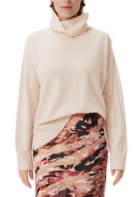 Jasno beżowy sweter z golfem, o luźnym kroju i długich rękawach. W połączeniu z wzorzystą spódnicą w ciepłych odcieniach.