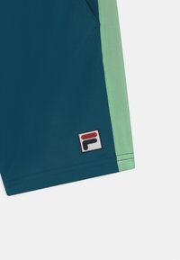 Tyrkysové šortky se zeleným síťovaným bočním panelem a vyšívanou nášivkou loga FILA na lemu. Vyrobené z lehkého, prodyšného materiálu.