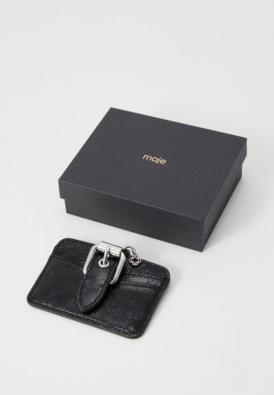 Portofel de carduri din piele neagră cu un finisaj texturat, accesorii din argint și un detaliu cu cataramă. Prezentat alături de o cutie neagră cu branding auriu.