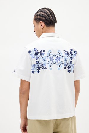 Hvid kortærmet skjorte med detaljeret blå blomsterbroderi på ryggen, med krave og afslappet pasform.