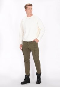Sweatshirt crème, pantalon cargo olive avec poches, bottes noires à lacets. Design simple, texture lisse, silhouette ajustée.