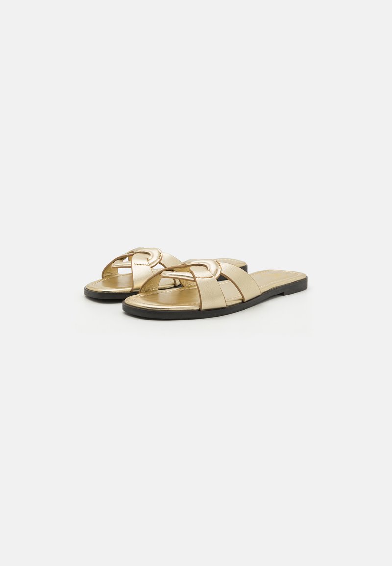Goldene, metallische Rutsch-Sandalen mit einem Kreuzband-Design, flacher Sohle und einem runden Akzent auf dem Schaft für zusätzliche Details.