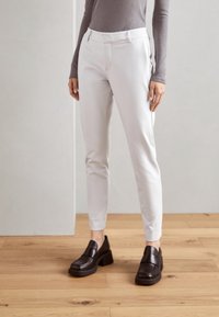 Vita skräddarsydda byxor med smal passform, elastisk midjeband och ankellängd, i kombination med mörkbruna kraftiga loafers på ett trägolv.