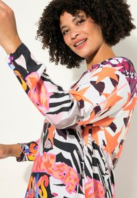 Langärmliges Kleid mit einem bunten abstrakten Muster in Pink-, Orange- und Schwarztönen. Glatter Stoff und Knopfdetail an den Säumen.