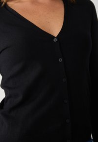 Black cardigan with a V-neck design, featuring a row of black buttons and a soft, textured knit. The fabric appears lightweight and smooth.