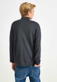 Maglione grigio scuro con colletto alto e maniche lunghe, abbinato a jeans azzurri chiari con cuciture evidenti e due tasche posteriori.