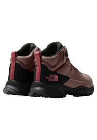 Botas de senderismo marrones y negras con un upper texturizado, cuello acolchado y acentos en rosa contrastante. Suela de goma gruesa con un patrón de tracción.