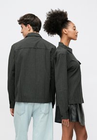 Czarne marynarki w cienkie prążki z kołnierzami, zestawione z jasnoniebieskimi dżinsami oraz czarną skórzaną spódnicą. Oba ubrania mają długie rękawy i guziki.