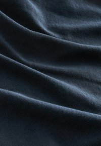 Tissu bleu foncé avec une texture fine et des plis doux créant des ombres et des reflets délicats sur la surface.