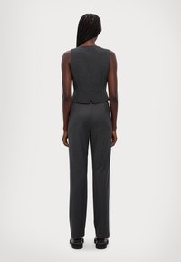 Mörkgrå ärmlös topp med vertikala ränder, parat med högmidjade, avsmalnande grå byxor. Snygg textur; minimalistiska skräddardetaljer.