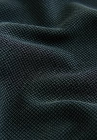 Nærbillede af mørkegråt stof med en tekstureret, lille kvadratisk gittermønster og bløde folder, der viser dybde og detaljer.