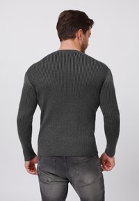 Grauer gerippter Pullover mit langen Ärmeln, strukturiertem Stoff, Rundhalsausschnitt und figurbetontem Design. Getragen mit grauen Jeans, von hinten betrachtet.
