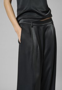 Pantaloni neri plissettati in tessuto liscio, con una vestibilità comoda, tasche laterali e vita piatta.