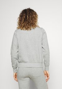 Sudadera gris heather con puños y dobladillo acanalados, que presenta un ajuste relajado y una textura suave. Detalles de costura visibles en el cuello.